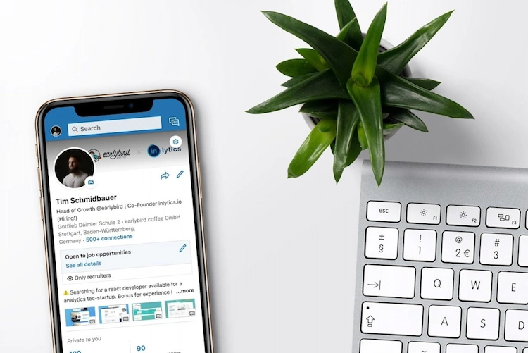 LinkedIn profile on iPhone on top of table beside plant and keyboard